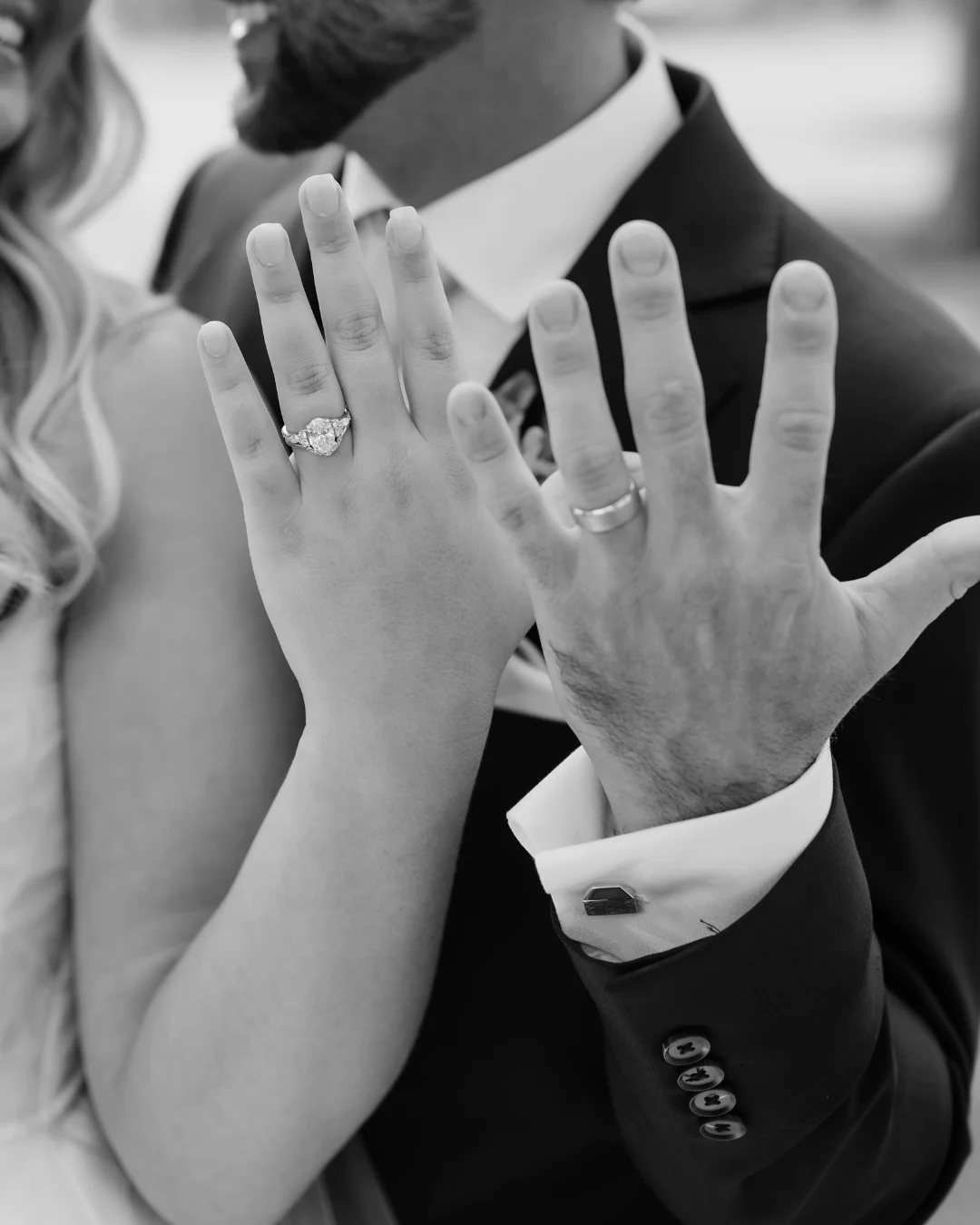 Black and white close-up of a couple showing their engagement ring and wedding band